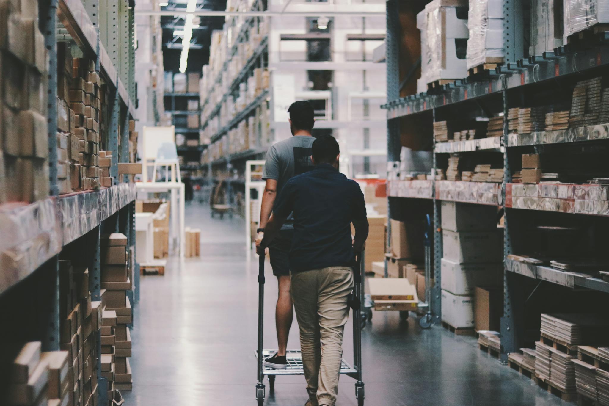 Image displays two individuals walking down an aisle in a warehouse.