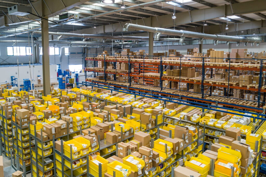 Image shows a warehouse with many boxes and holding trays on multiple racks. Image is taken with a birds-eye view.