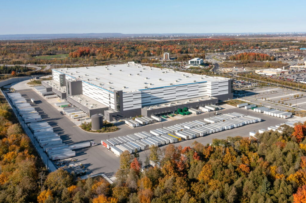 Image displays a building surrounded by many colorful trees over many acres. A city appears in the distance.